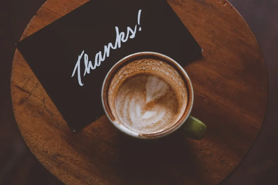 thank you written in white on black card with coffee next to it
