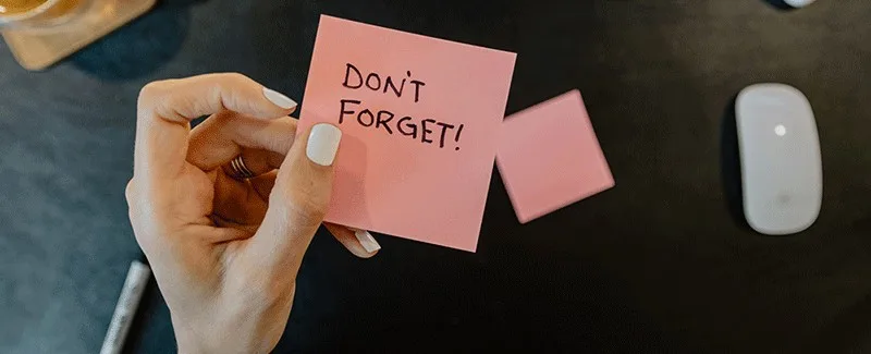 don't forget written on a pink postit note and held over a black desk 